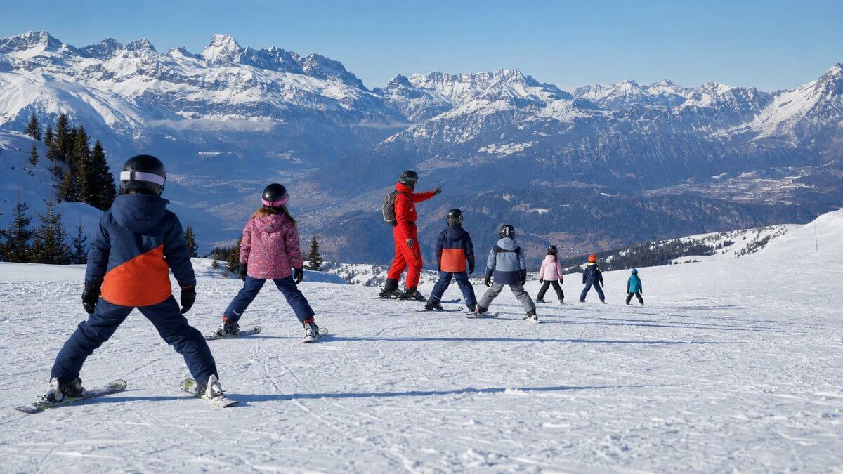 Un groupe d'enfants progresse à ski avec un moniteur dans les Alpes