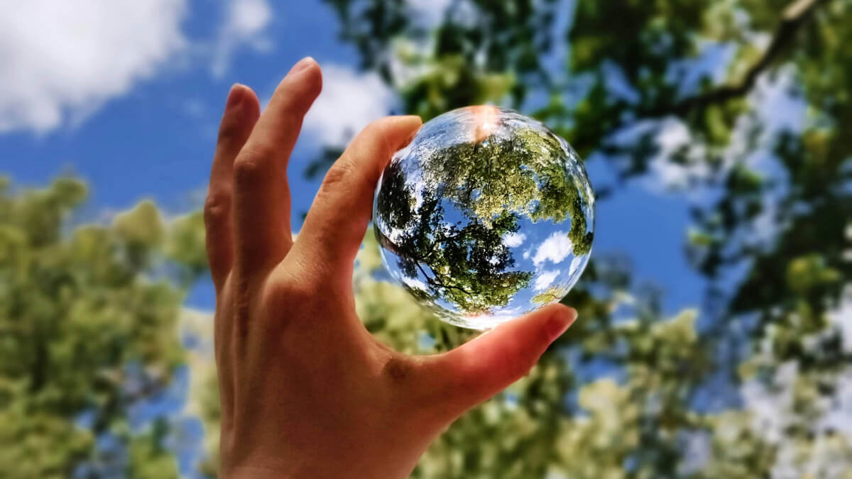 Main tenant une sphère de verre qui reflète des arbres et le ciel